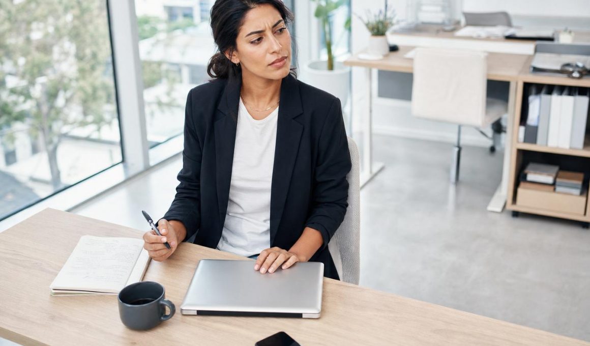 Femme réfléchissant à son bureau avec ordinateur portable