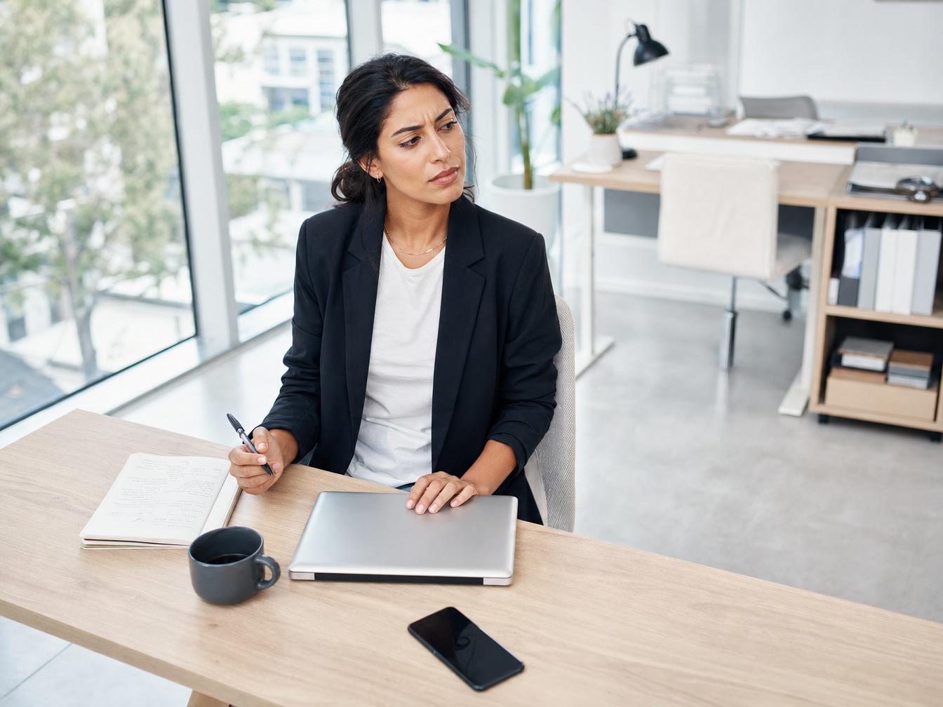 Femme réfléchissant à son bureau avec ordinateur portable